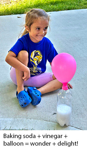 Girl smiles with delight at her camp guide and mentor as a solution of vinegar and baking soda in a bottle reacts, giving off gas that inflates a balloon attached to the top of the bottle
