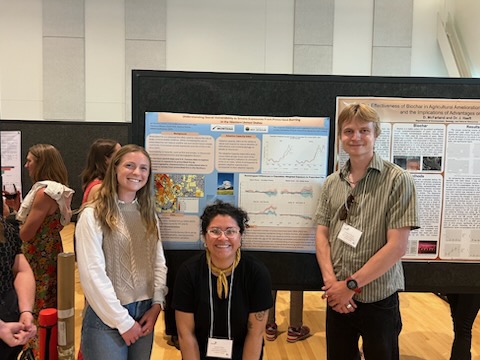Three people smiling and standing in front of two science posters