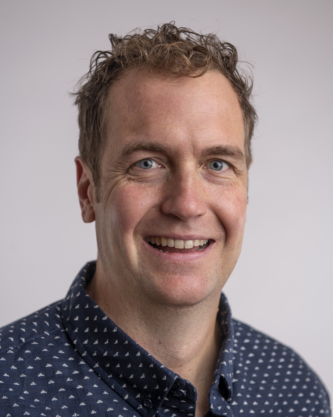 Headshot of John Chandler in a blue collared shirt
